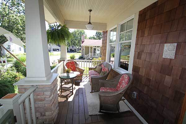 The covered front porch is furnished with a round side table and wicker round back chairs sitting on a beige area rug.