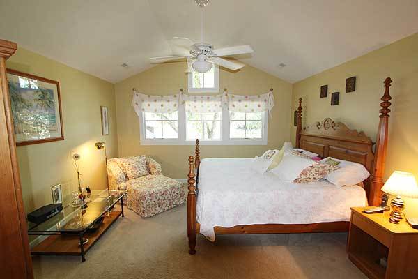 Primary bedroom with cathedral ceiling, carpet flooring, and yellow walls adorned with various artworks.