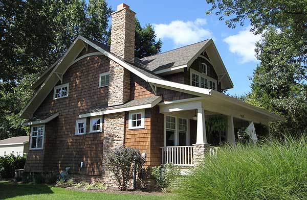 Home's side view showing the brick exterior, white-framed windows, and a stone chimney.