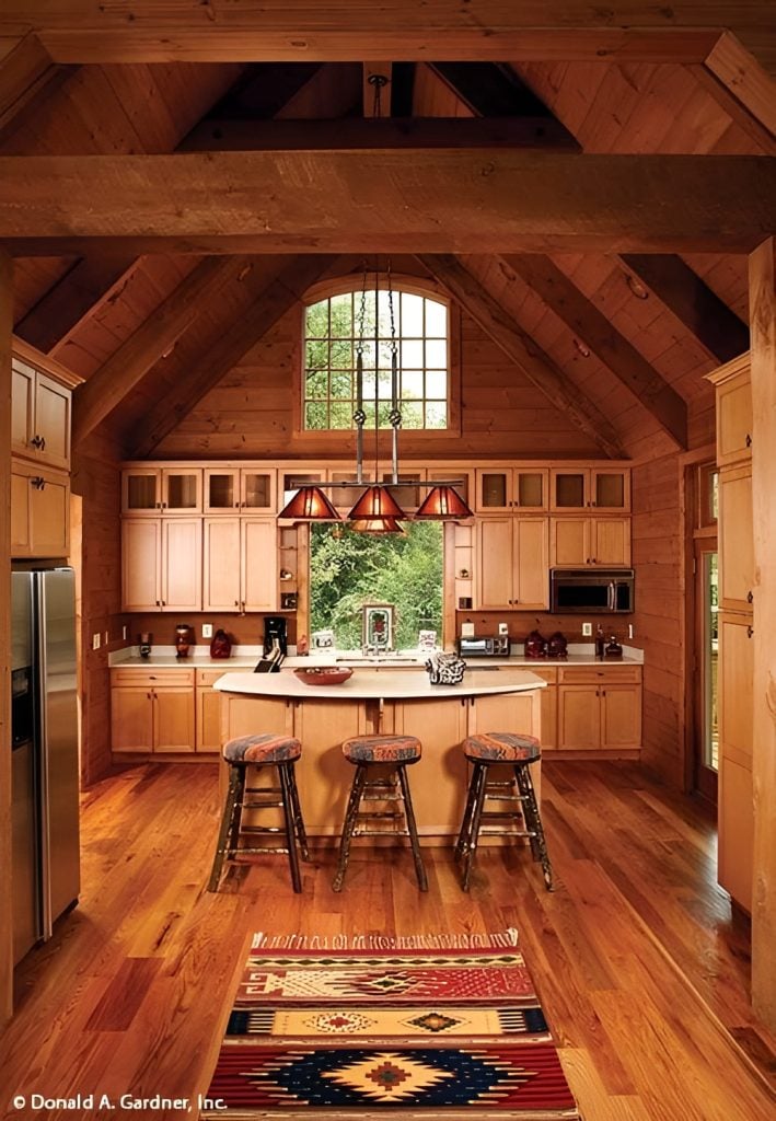 The kitchen has light wood cabinets, a tasseled tribal rug, and a breakfast bar lined with round bar stools and glass pendants.