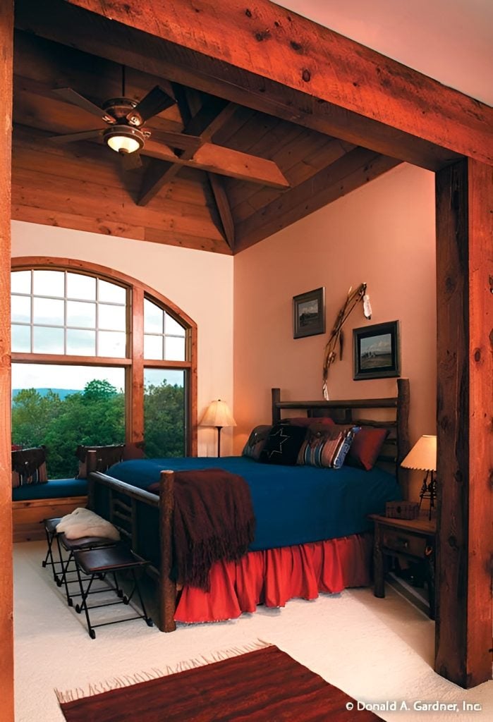 The primary bedroom features a window seat and a skirted bed complemented with wooden nightstands and wrought iron footstools.