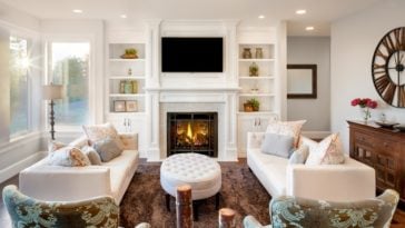 This family room has a consistent white tone to its ceiling and walls that has built-in shelves and cabinets flanking the fireplace with a white mantle.