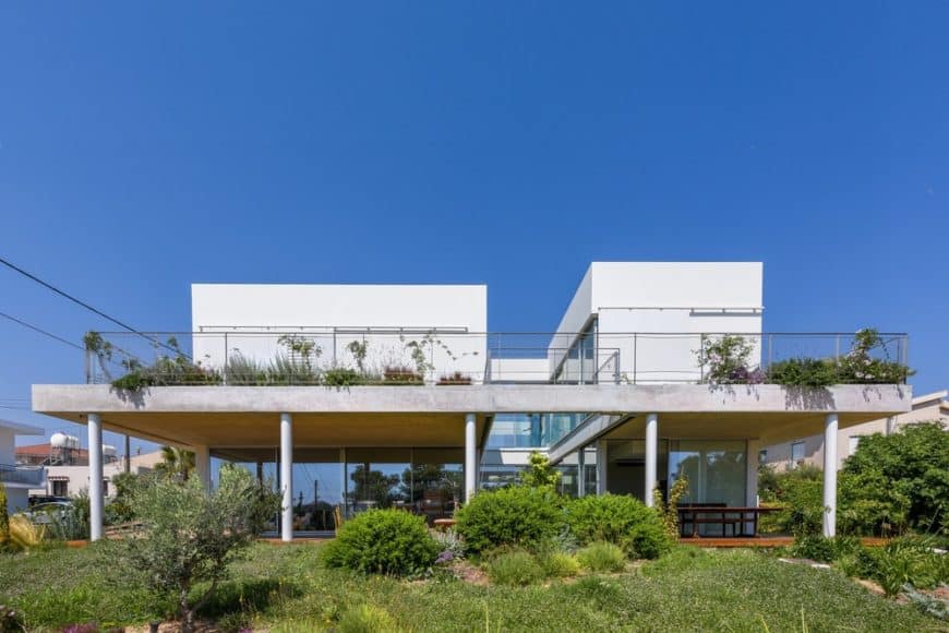 This is a bright and white house with two large structures connected by the glass walls of the ground floor and the large balcony of the second floor adorned by the landscape on both levels.