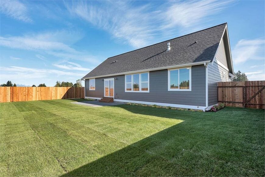 Angled rear view showing the open patio and an expansive lawn surrounded by a wooden fence.