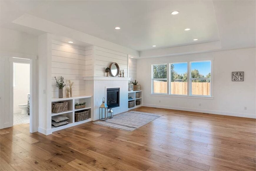 The living room has triple pane windows and a glass-enclosed fireplace flanked with white built-ins.