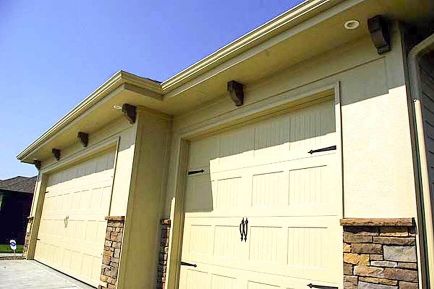 The three-car garage is adorned with brick accents and decorative wooden brackets.