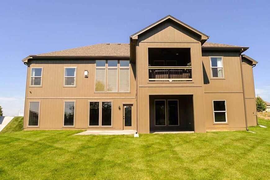 Rear exterior view with vertical wood siding and an upper balcony enclosed in wrought iron railings.