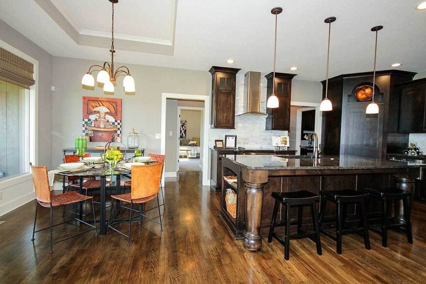 Eat-in kitchen with dark wood cabinets, granite countertops, and a large center island well-lit by glass dome pendants.