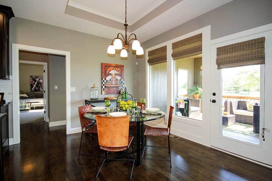 The dining area offers a glass chandelier, round dining table, woven chairs, and a metal buffet bar placed under the lovely artwork.