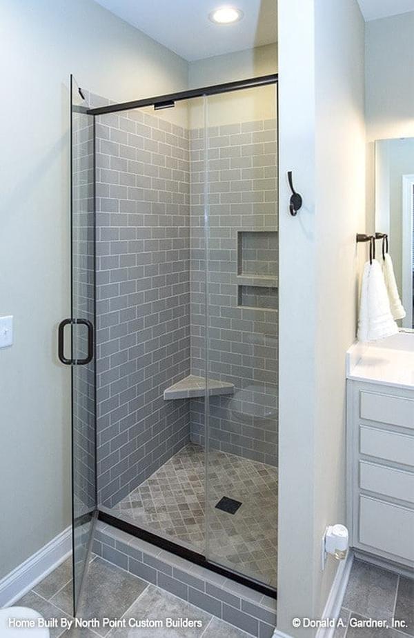 The walk-in shower features gray subway tile walls fitted with inset shelves and a corner tiled seat.