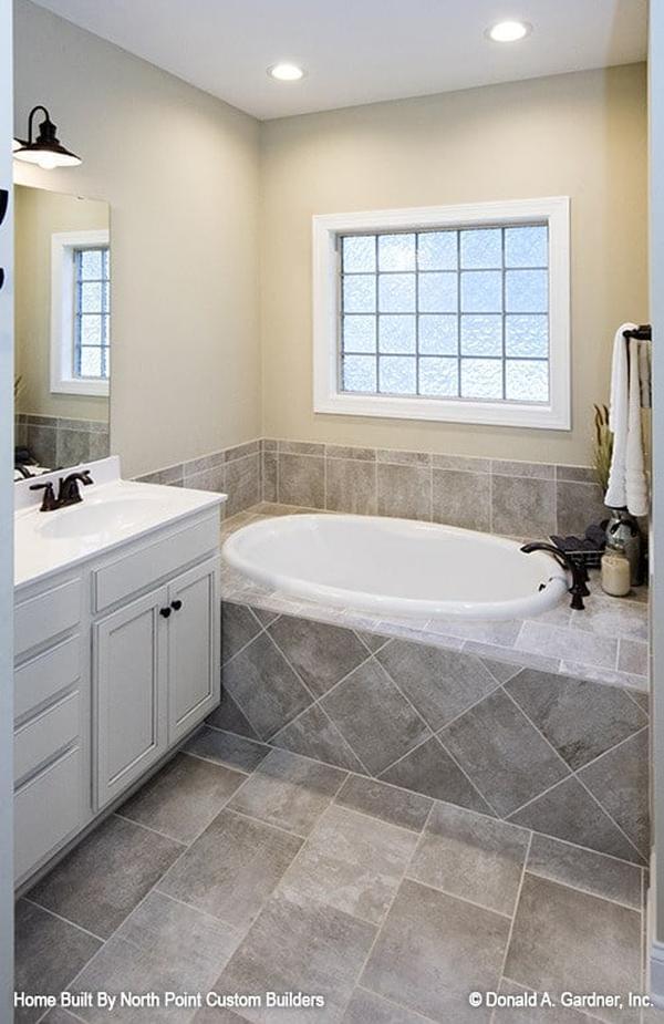 Primary bathroom with white sink vanity and a deep soaking tub fixed under the glass block window.
