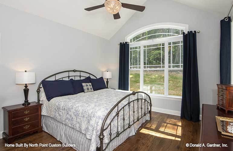 Primary bedroom with dark wood cabinets, metal bed, and an arched window dressed in deep blue draperies.