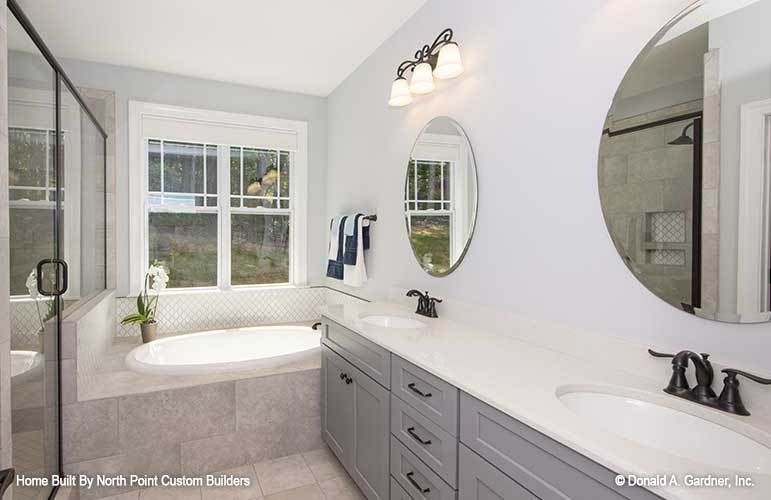 The primary bathroom offers a walk-in shower, a drop-in bathtub, and a dual sink vanity placed under the round frameless mirrors.