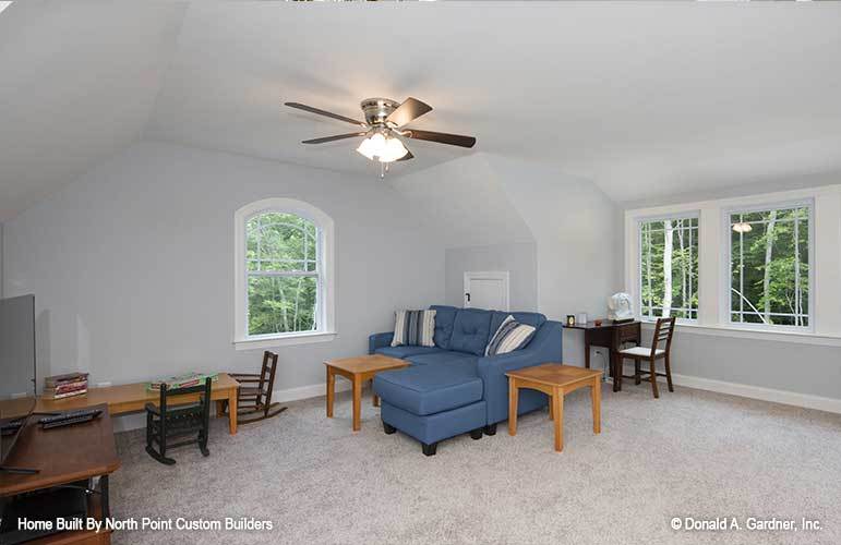 Spacious bonus room filled with wooden tables, an L-shaped sofa, and a flatscreen TV.