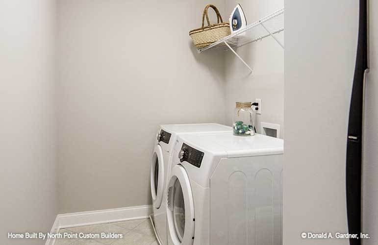 Utility room with tiled flooring, white front-load appliances, and a white metal shelving.