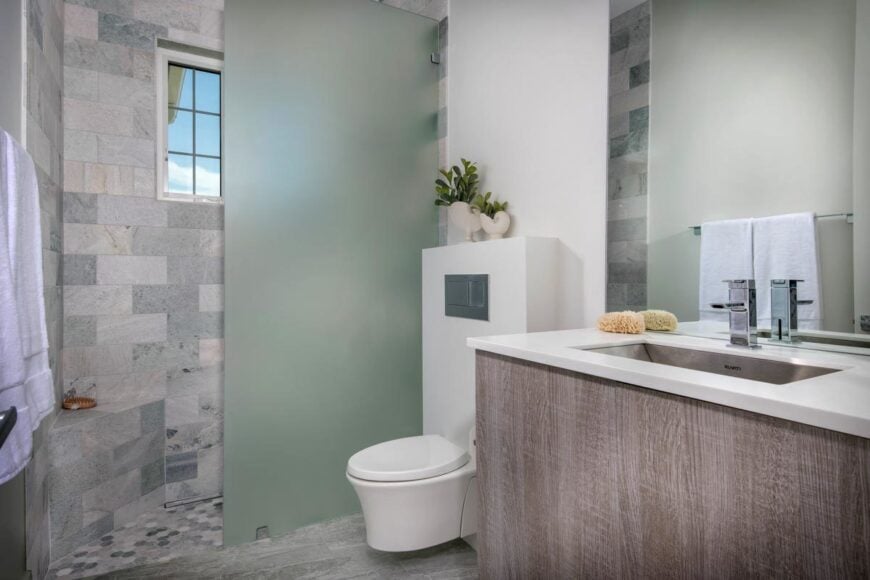 Bathroom with a sink vanity, wall-hung toilet, and a walk-in shower enclosed in a frosted glass panel.