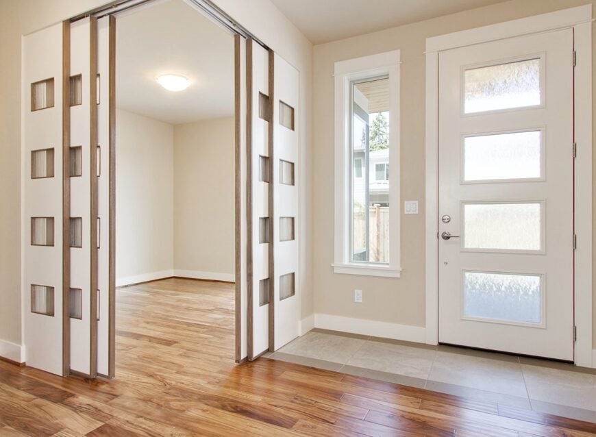 Foyer with a white entry door and natural hardwood flooring. Sliding doors on the side open to the den.
