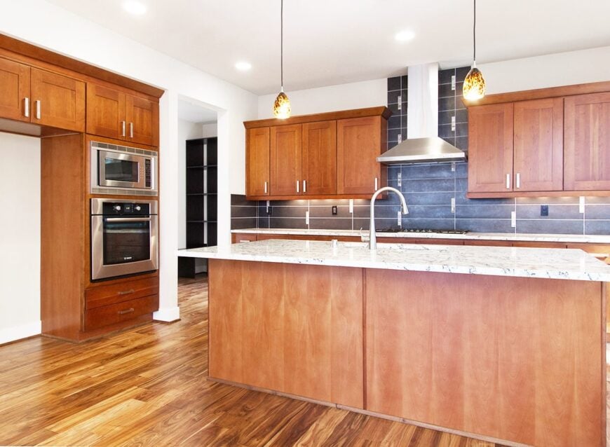 The kitchen is equipped with stainless steel appliances, marble countertops, wooden cabinetry, and an undermount sink fitted on the central island.