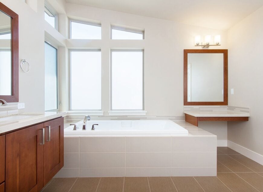 Next to the bathtub is a built-in vanity with a quartz countertop and a wooden framed mirror.