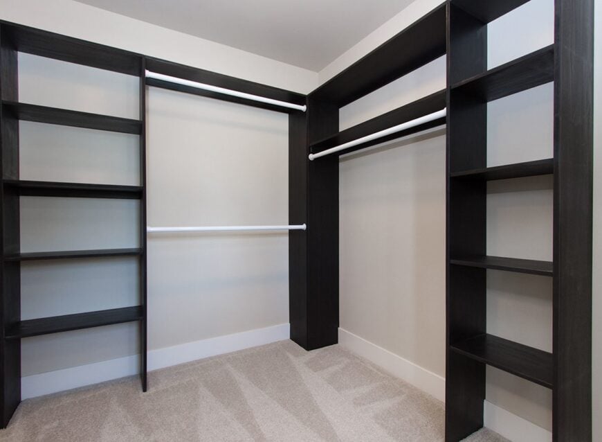 The walk-in closet is filled with black shelvings and built-in pole racks.