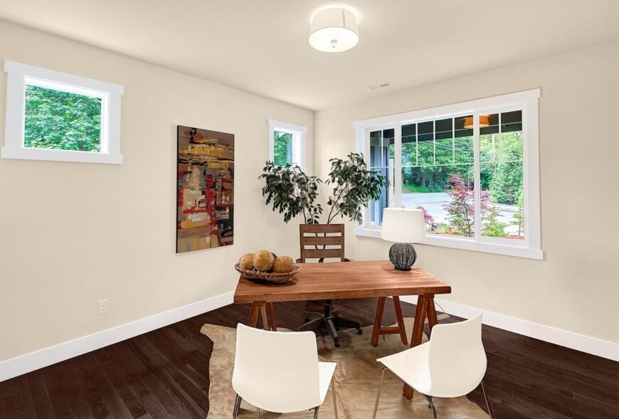 The study is furnished with a wooden desk, a matching swivel chairs, and a pair of white contemporary chairs sitting on a cowhide rug.