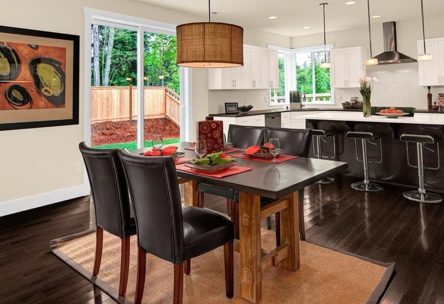 Breakfast nook with a jute rug, leather high back chairs, and a wooden dining table illuminated by a drum chandelier.