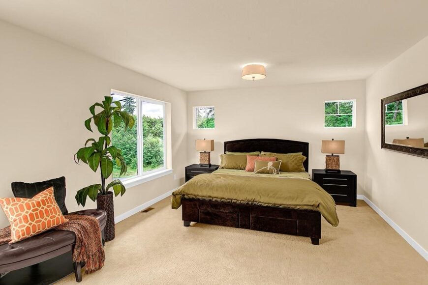 Primary bedroom with a tufted leather bench, rectangular wall mirror, and a cozy dark wood bed flanked by matching nightstands.