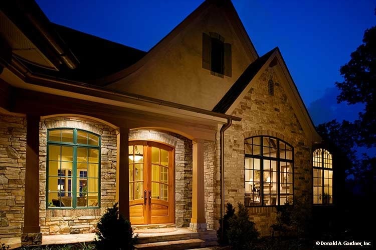 Front view of the house with stone exterior, a french entry door, and a covered porch framed with wooden columns.