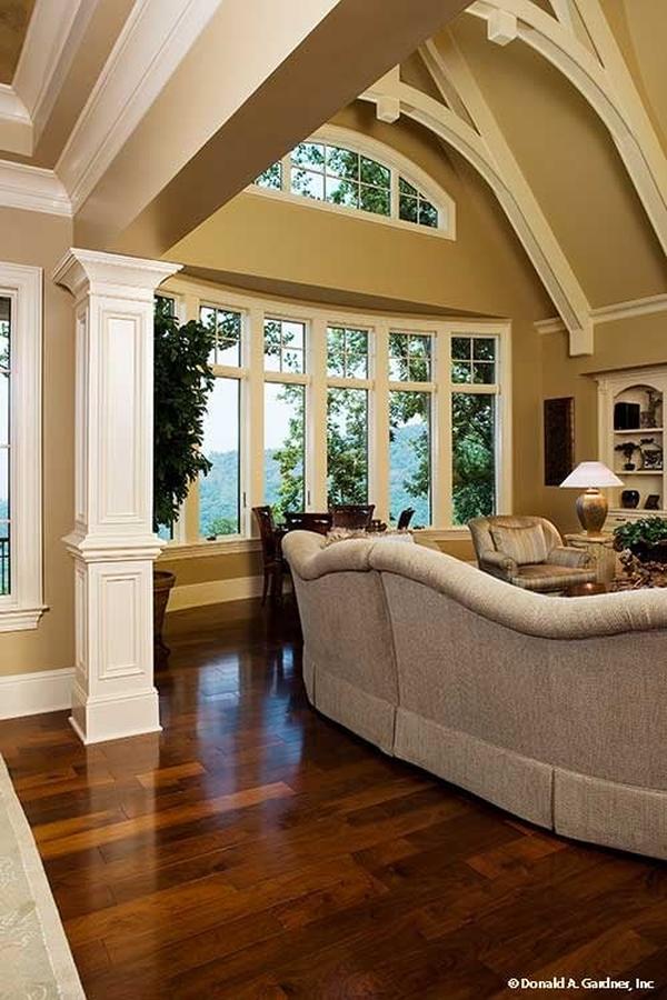 The living room has rich hardwood flooring, a bow window, and a cathedral ceiling lined with decorative white beams.