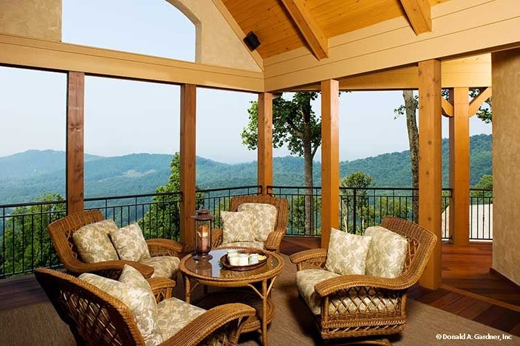 The screened porch showcases wicker armchairs, a matching table, and a breathtaking mountain view.