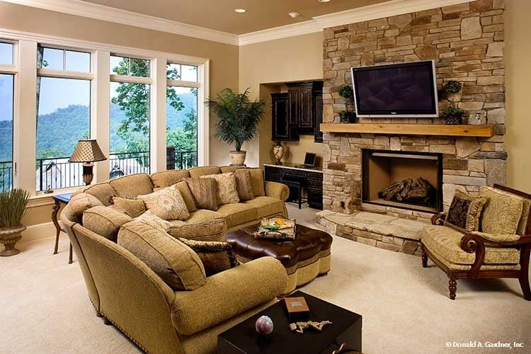 The entertainment room offers an L-shaped sofa, cushioned armchair, and a stone fireplace with a wall-mounted TV on top.
