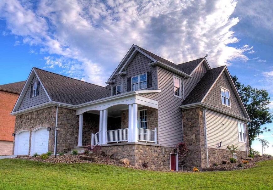 Side exterior view showing the double garage and a covered porch enclosed in white railings and double columns.
