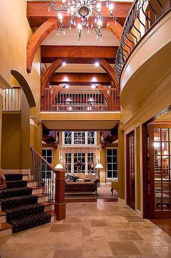 The foyer has an ornate chandelier and a traditional staircase dressed in a patterned carpet.