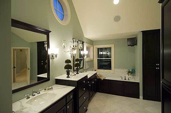 Primary bathroom with a dual sink vanity, a drop-in bathtub, and a small TV mounted against the sage green wall.