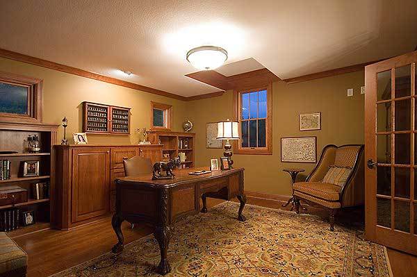 The home office has a carved wood desk, cozy chairs, and wooden built-ins that blend in with the rich hardwood flooring.