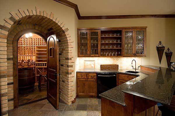 Wet bar with a two-tier peninsula, natural wood cabinets, and a wine fridge. An arched doorway on the side leads to the wine cellar.