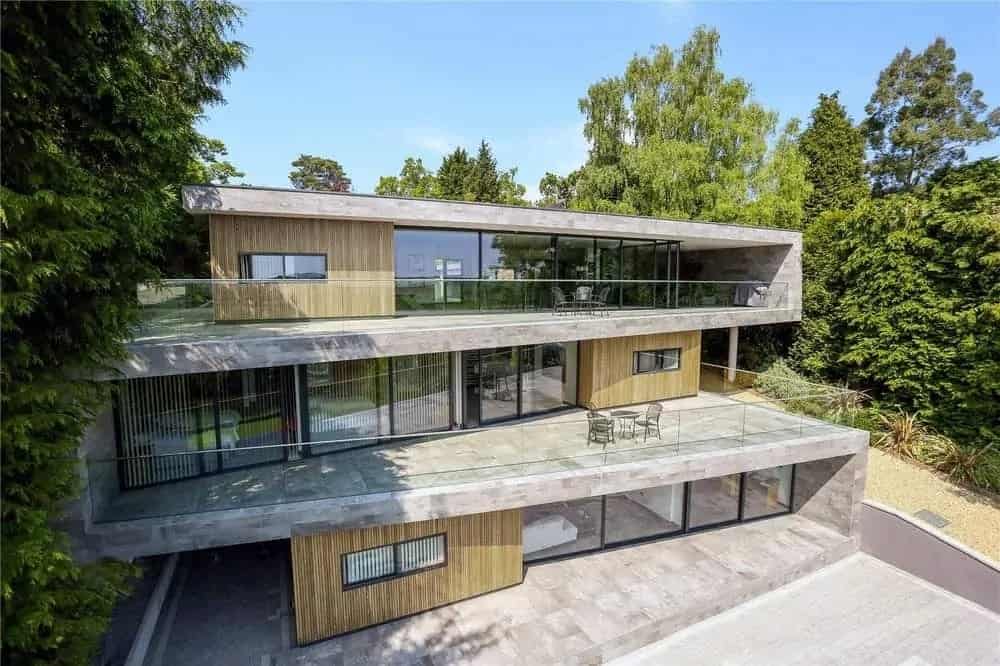 This is an aerial view of the house that showcases three levels of concrete, glass walls and sliding doors complemented by a few wooden walls that match well with the surrounding tall trees.