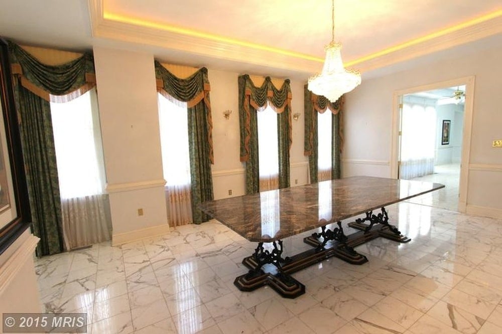 The large dining table of the dining room is illuminated by the warm light of the pendant light and the natural lights coming in from the row of tall windows. Image courtesy of Toptenrealestatedeals.com.