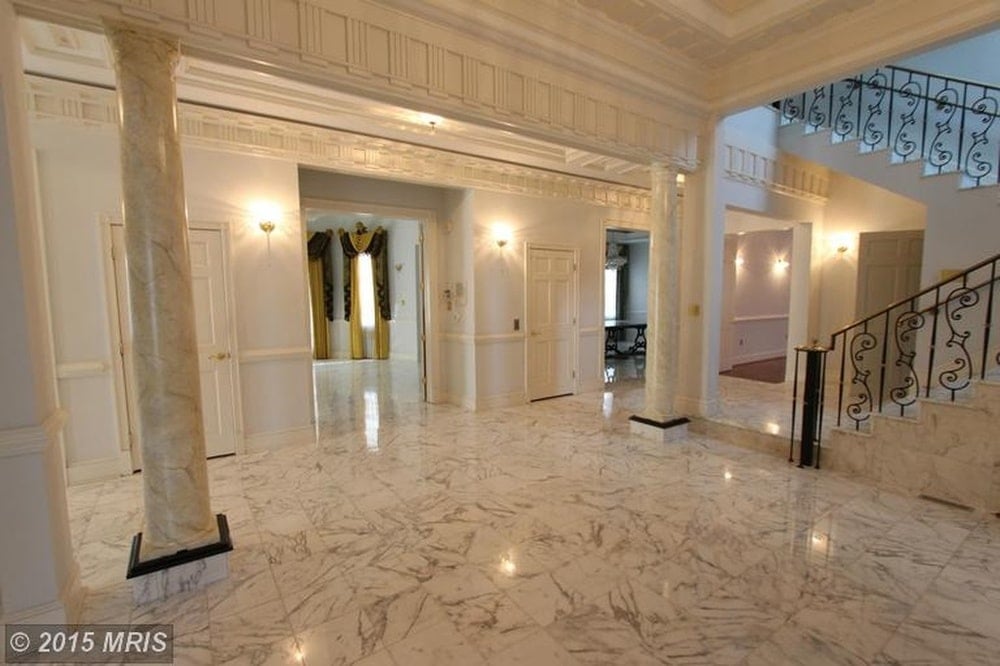 Upon entry of the house, you are welcomed by this foyer with a spacious white marble flooring adorned with pillars and warm lights on the walls. Image courtesy of Toptenrealestatedeals.com.