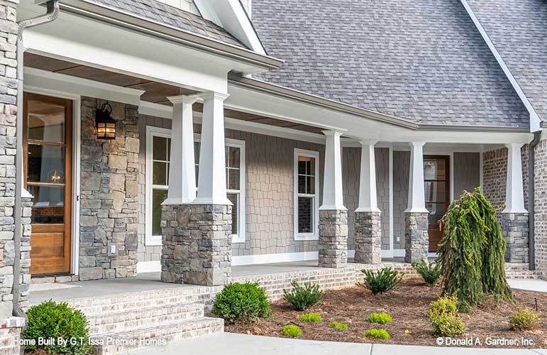 Home's entry showing the wooden front door and a wide porch lined with tapered columns.
