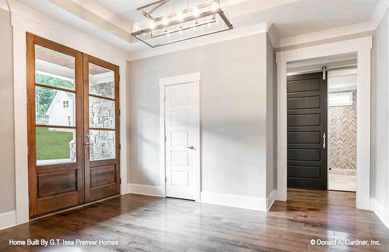 The foyer has a wooden french entry door and a large chandelier that hangs from the tray ceiling.