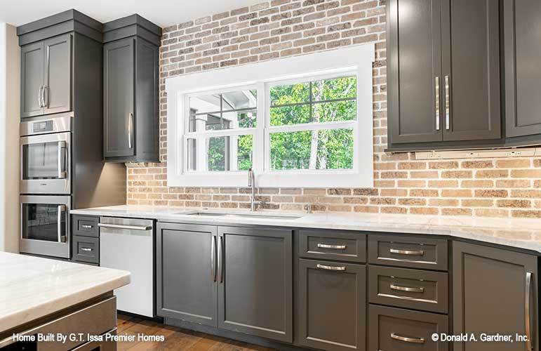White marble countertops, stainless steel appliances, and dark wood cabinetry against the brick backsplash fill the kitchen.
