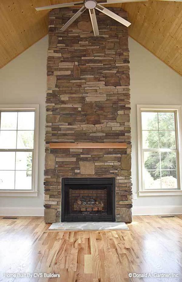 Spacious sitting room with a stone fireplace and a ceiling fan mounted on the cathedral ceiling.