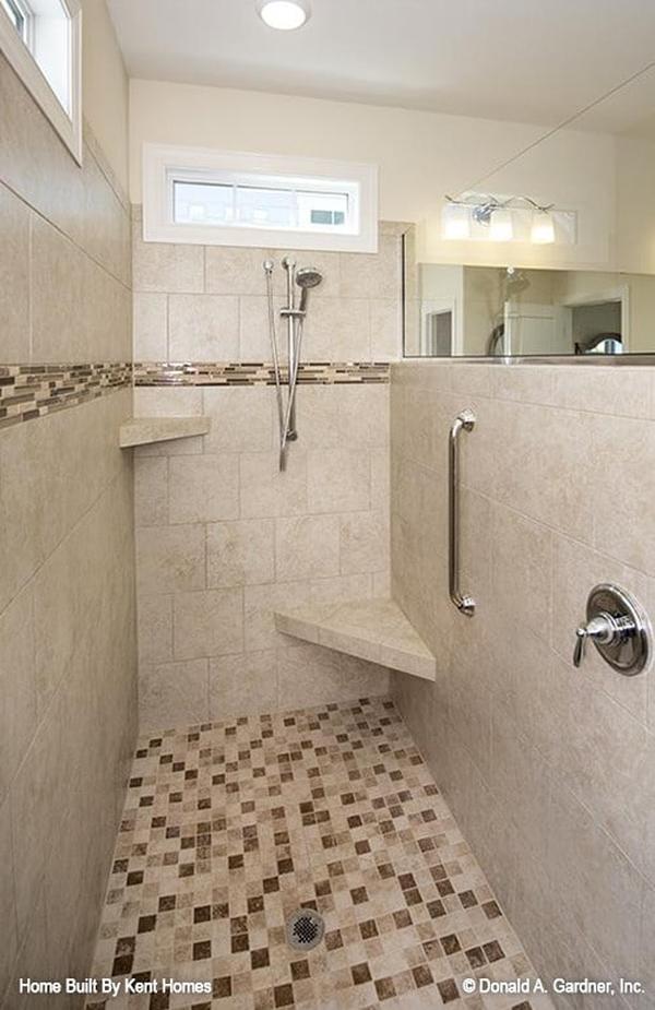 Walk-in shower with beige marble tiled walls, corner shelves, chrome fixtures, and mosaic tiled floor.