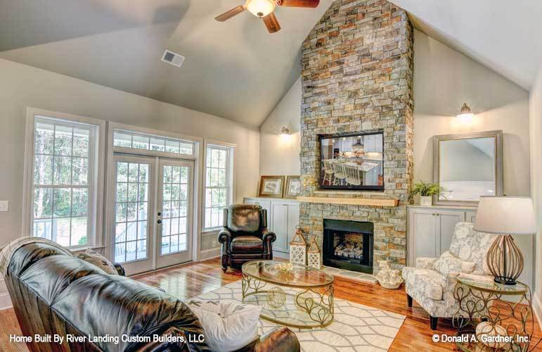 The living room offers black leather and floral seats, glass top tables, and a stone fireplace flanked with white cabinets.