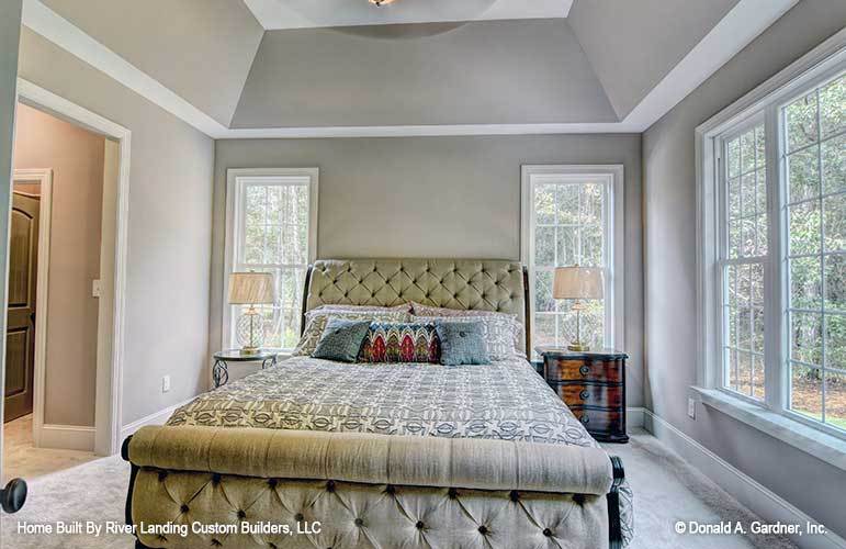 Primary bedroom with a coved ceiling, gray carpet flooring, and a beige tufted bed nestled in between the ornate and wooden nightstands.