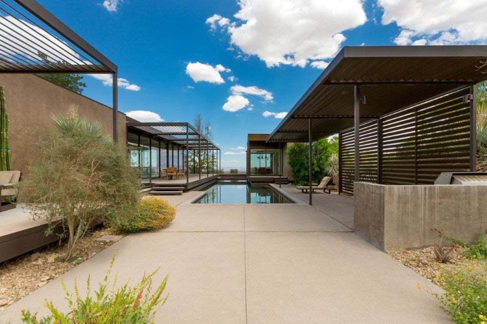 This is a look at the back of the house with a large pool, concrete walkways and steel structures that have an earthy tone. Image courtesy of Toptenrealestatedeals.com.