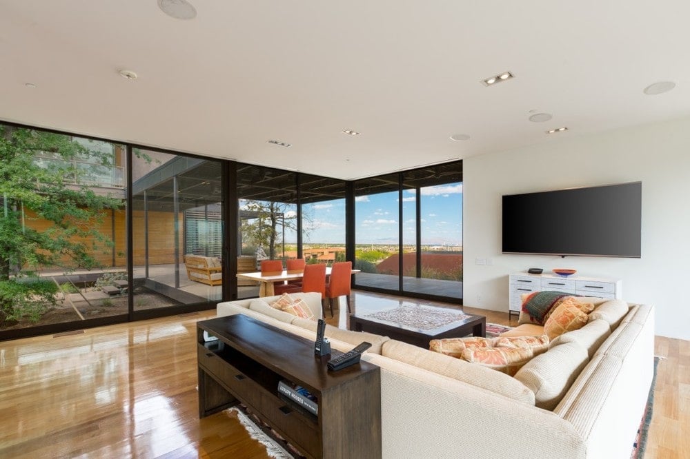 This is the bright and airy family room with a large L-shaped sectional sofa to match the beige walls and ceiling. These are then contrasted by the hardwood flooring and the black frames of the glass walls. Image courtesy of Toptenrealestatedeals.com.