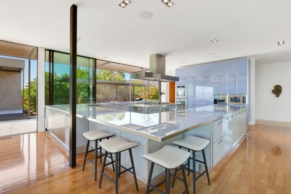 This is the large kitchen of the house with a large U-shaped peninsula adorned with frosted glass cabinetry and matching countertop that has a breakfast bar at the corner. Image courtesy of Toptenrealestatedeals.com.