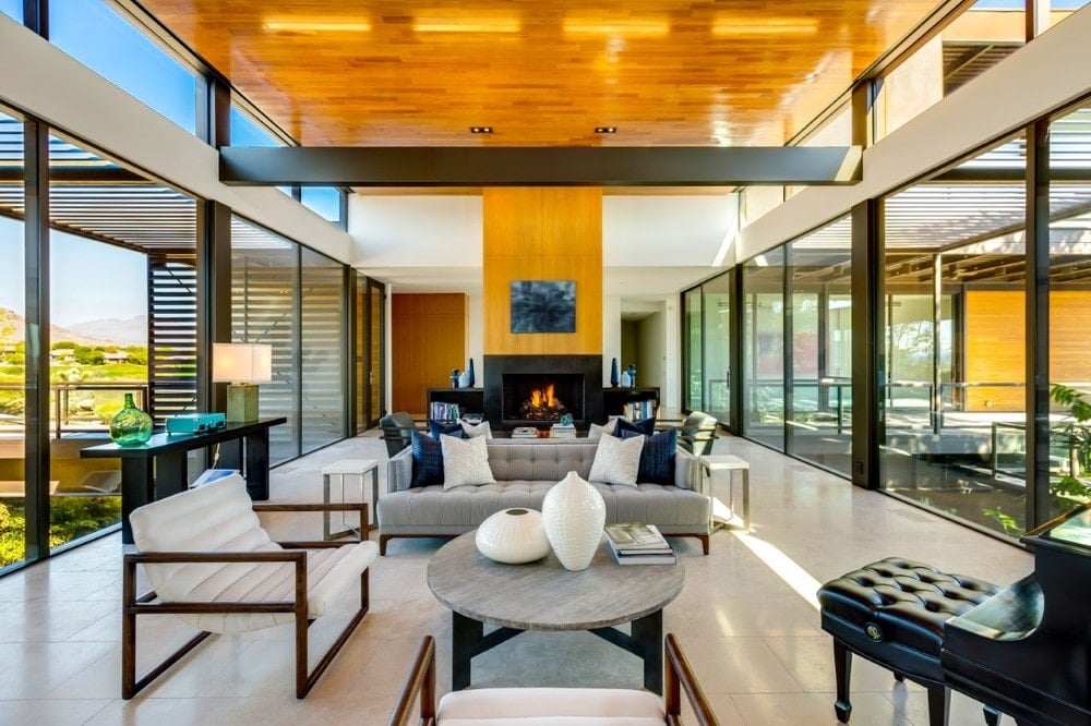 This is a spacious living room with a tall wooden ceiling complemented by the exposed metal beam and the glass walls on two sides that bring in an abundance of natural lighting. Image courtesy of Toptenrealestatedeals.com.